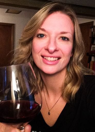 Smiling woman with wavy blonde hair holding a large glass of red wine