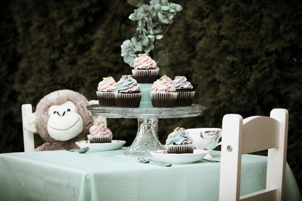 Decorated cupcake stand with pink frosted cupcakes and floral arrangement set up for a professionally catered children's party or private event