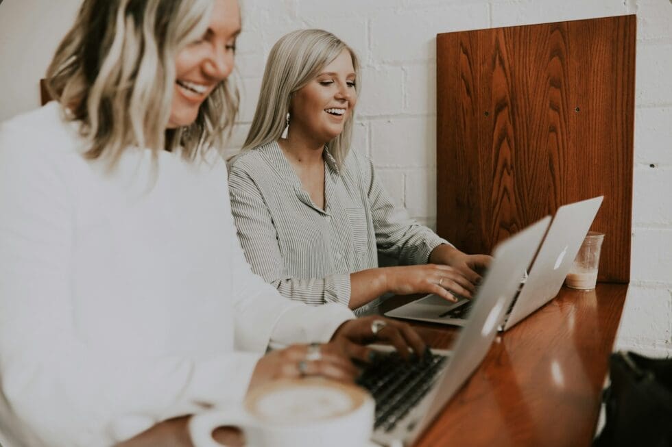 Two smiling hospitality staffing professionals collaborating on a laptop to plan and coordinate an upcoming client event