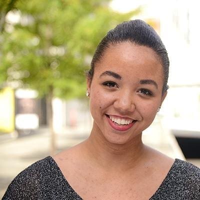 Smiling young woman with hair pulled back, photographed outdoors with a blurred street background
