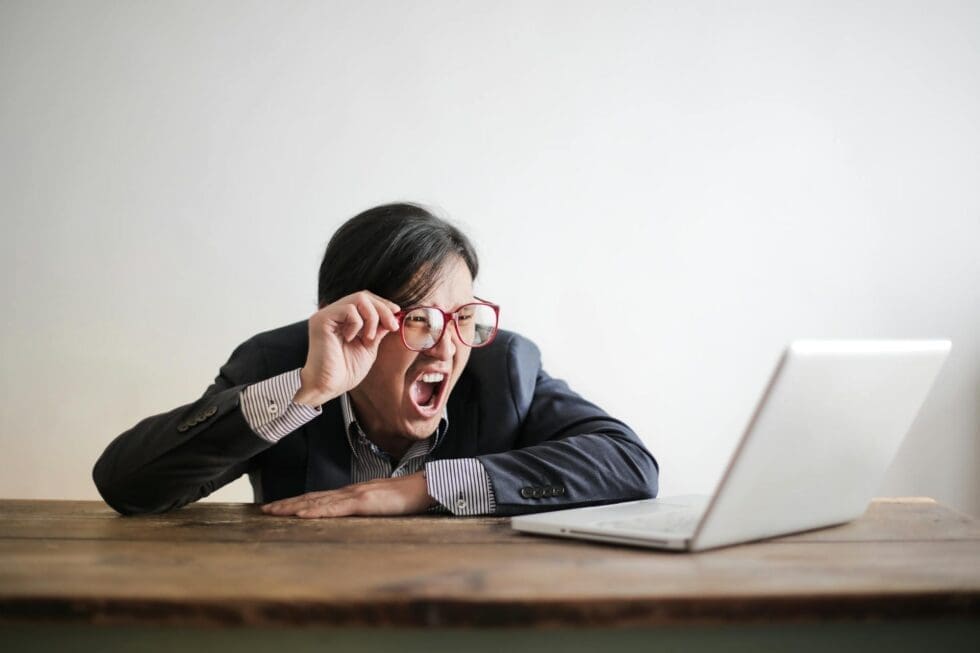 frustrated-man-yelling-at-laptop-hmg-plus Frustrated event planner reacting to understaffing problems at a corporate event, solved by HMG+ professional staffing services