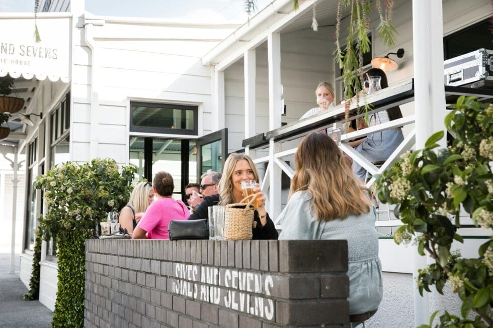 Guests enjoying drinks at an outdoor restaurant patio with professional hospitality service staff assisting in a relaxed, upscale dining setting.