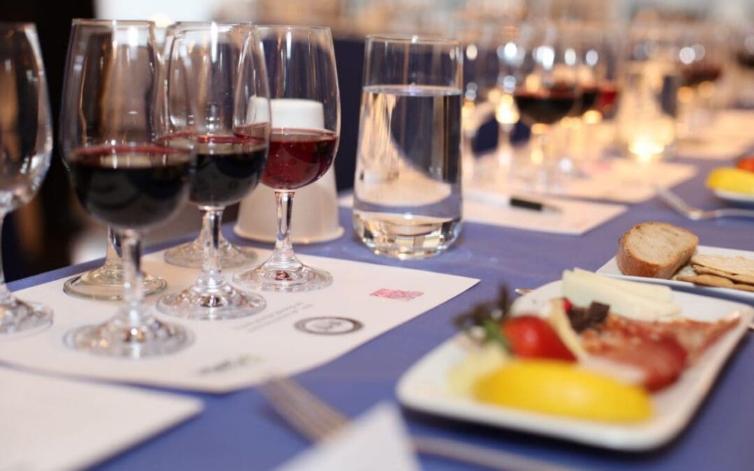 Elegant wine tasting setup with multiple red wine glasses, water glasses, and a cheese and charcuterie plate arranged on a blue tablecloth